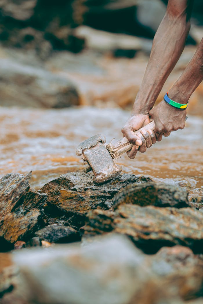 Close-up of a person breaking rock with a hammer, showcasing manual labor outdoors.