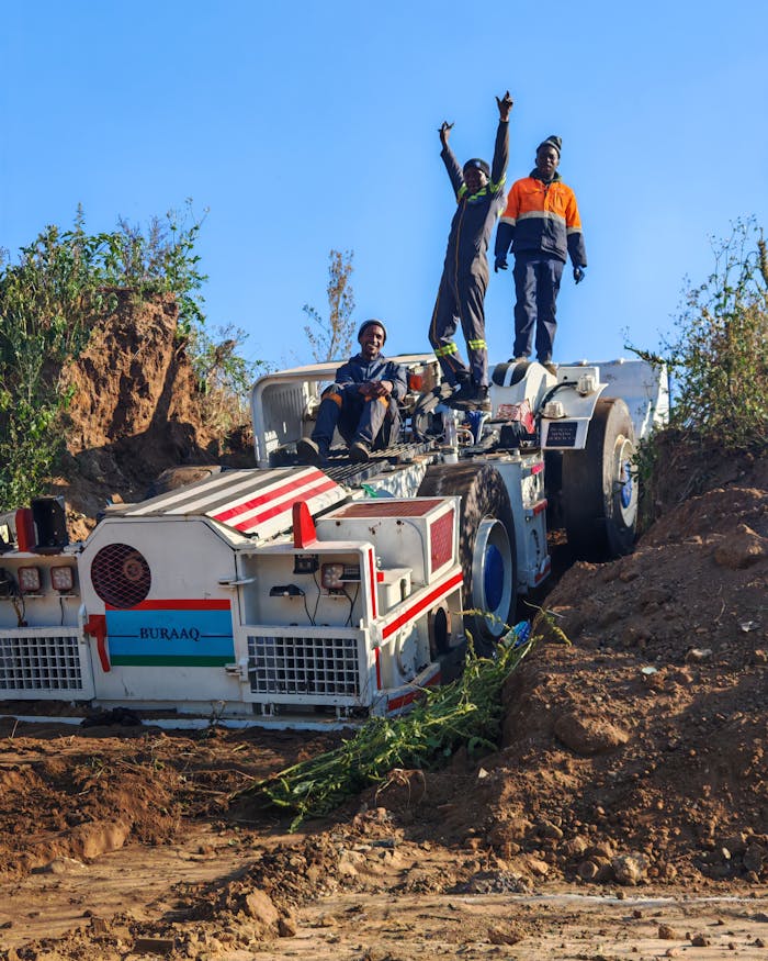 Workers standing triumphantly on mining machinery in Johannesburg, South Africa under a clear blue sky.